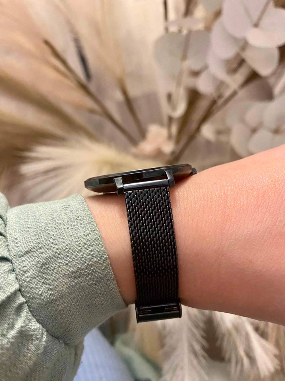 Seitenansicht auf die schwarze getestete Damenuhr, die mittel Gliederarmband an einem Handgelenk befestigt ist.