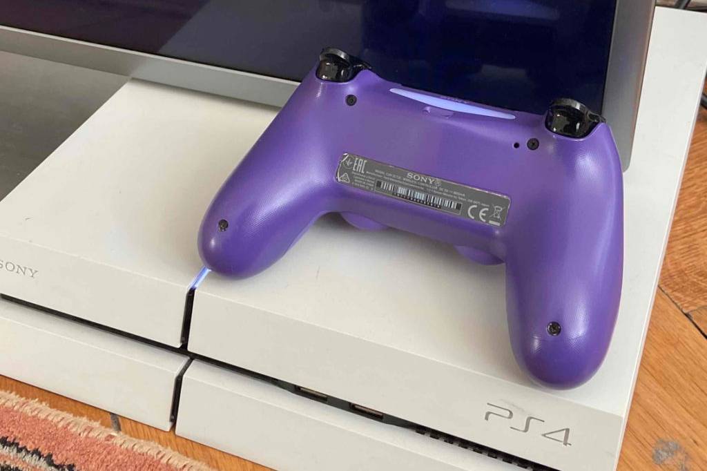 Ein getesteter PS4-Controller liegt umgedreht auf einer Konsole vor einem Fernseher.