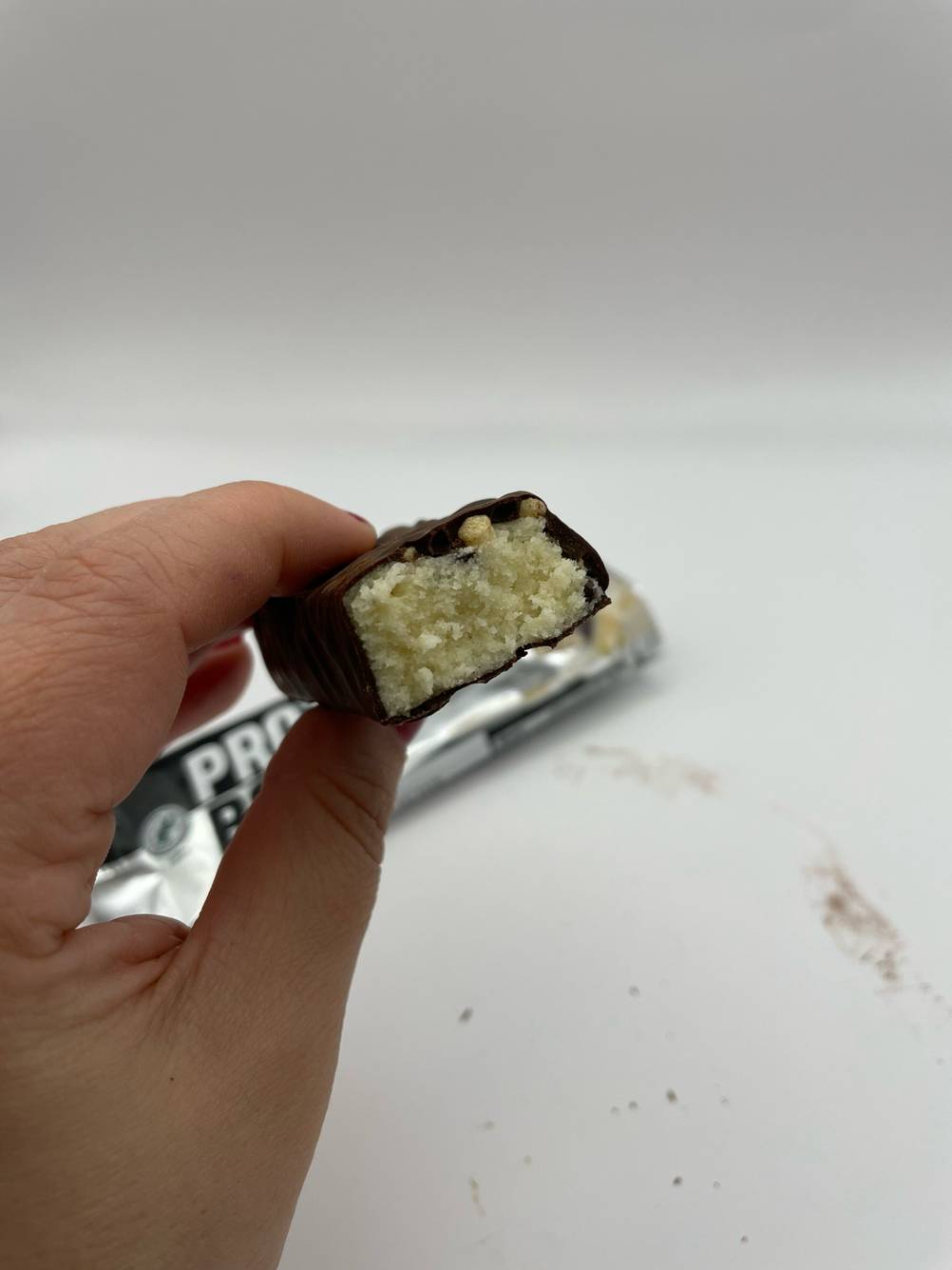 Der getestete Weider-Proteinriegel wird in der Hand gehalten, wobei ein Stück abgebrochen wurde, damit die Füllung des Riegels ersichtlich ist.