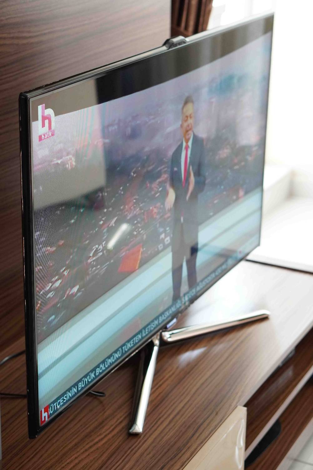 Eingeschalteter, getesteter Fernseher steht auf einem braunen Holztisch in der Seitenansicht.