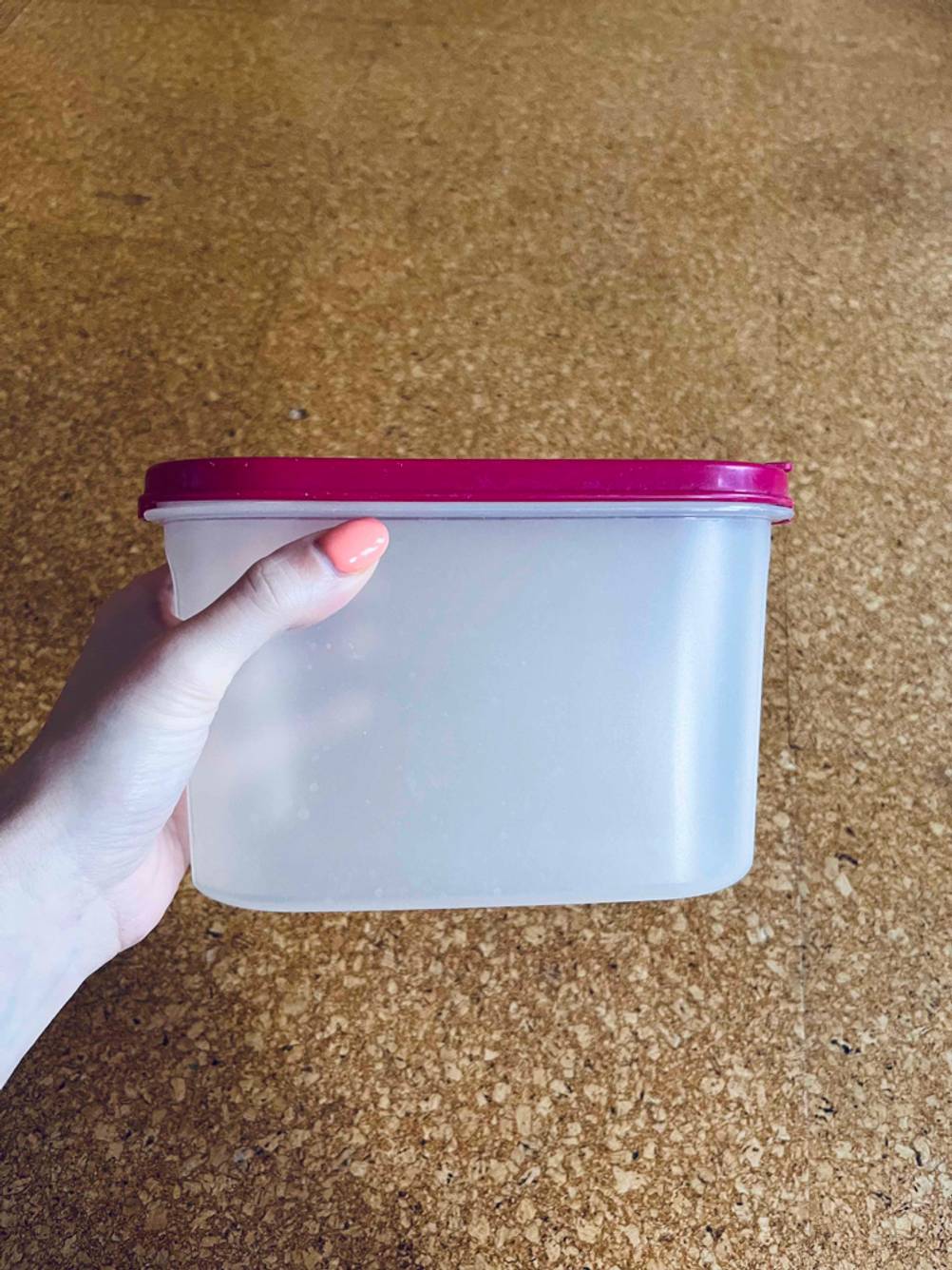 Im Test: Eine Hand hält eine Tupperware mit pinkem Deckel vor eine Holzfläche.
