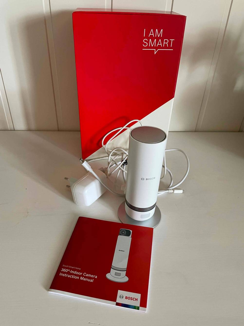 Alle Zubehörteile einer getesteten 360 Grad Kamera liegen vor der Originalverpackung vor einer hellen Wand.