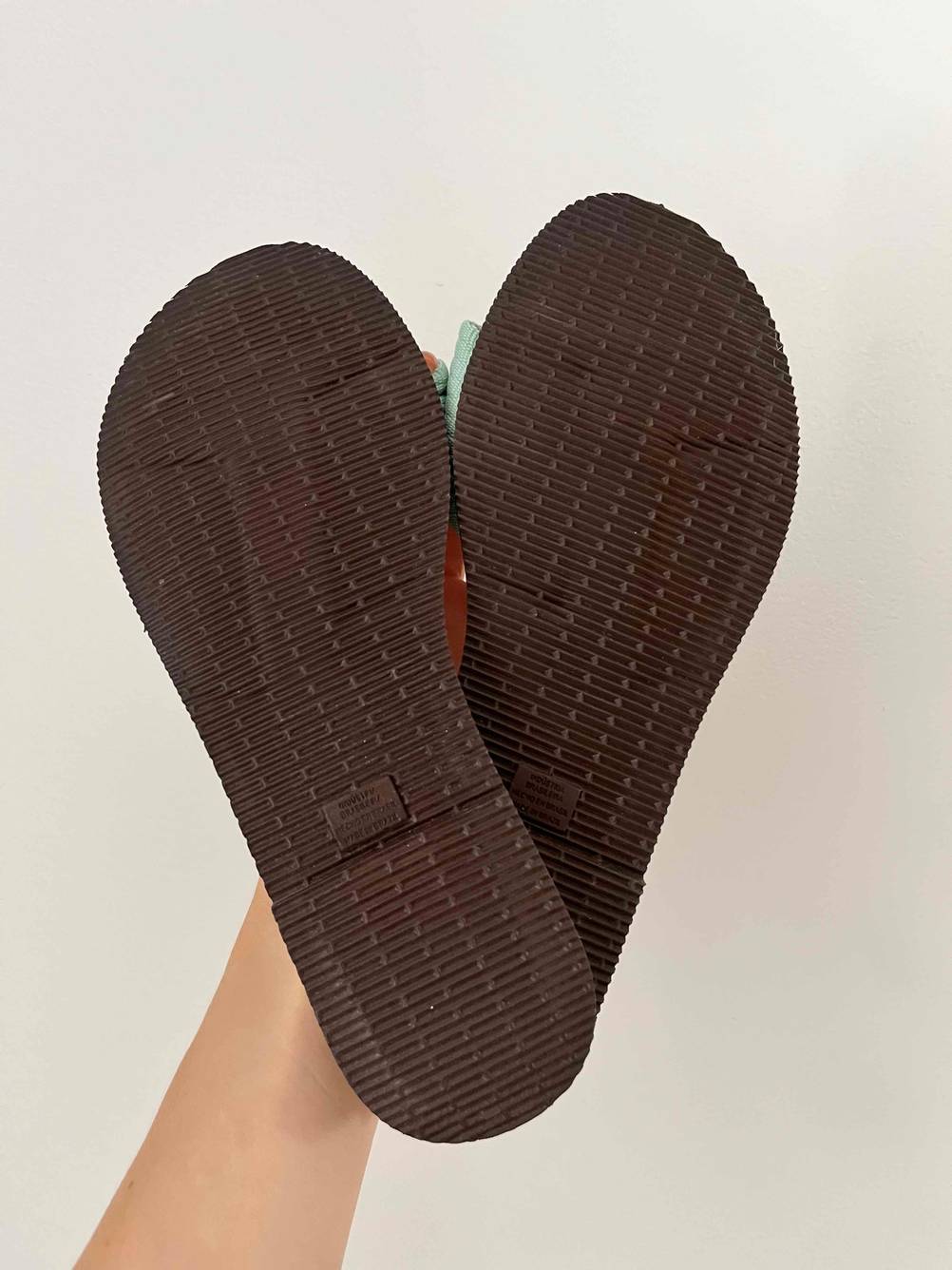 Im Test: Eine Hand hält ein Paar Pantoletten für Damen mit der Sohle nach vorne vor eine helle Wand.
