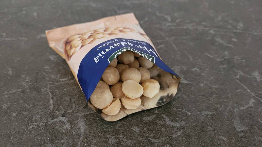 Im Test: Eine geöffnetet Packung Macadamia-Nüsse auf einer dunklen Fläche.