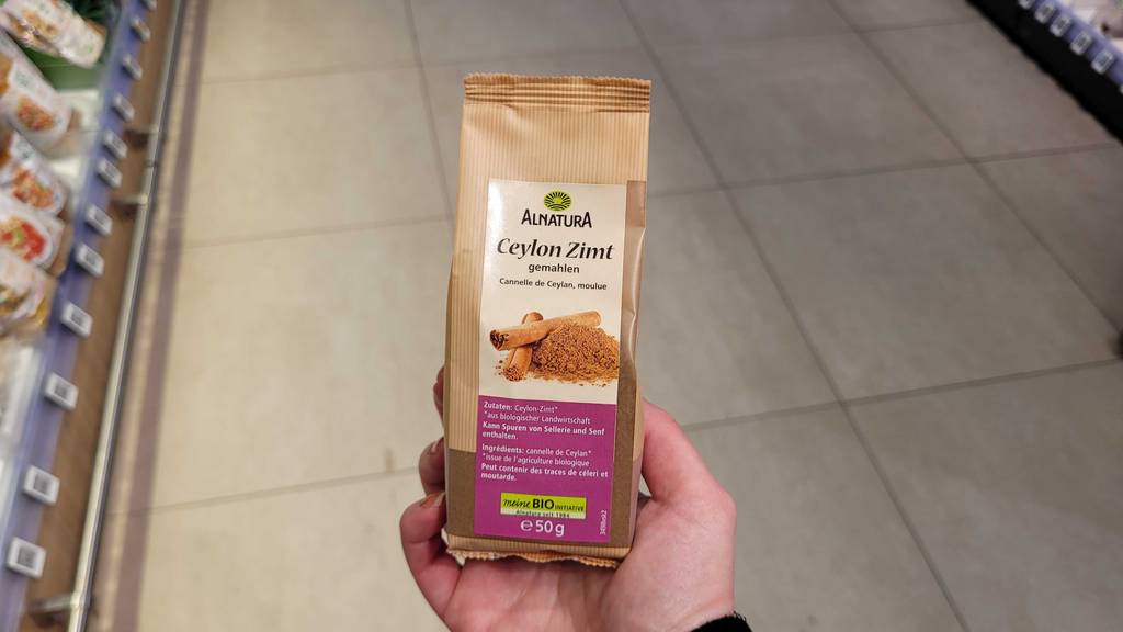 Eine Hand hält eine 50-g-Packung mit Ceylon-Zimt im Test neben einem Verkaufsregal.