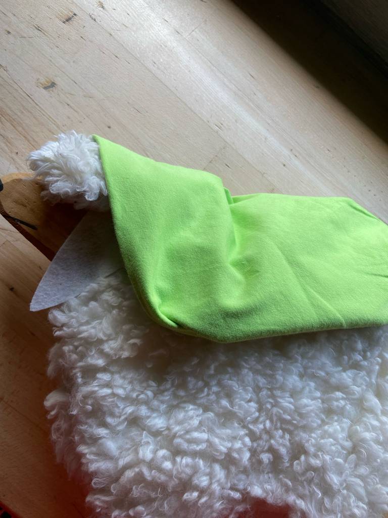 Beanie-Test: Eine grüne Mütze liegt auf einem weißen Kunstlanghaarfell.