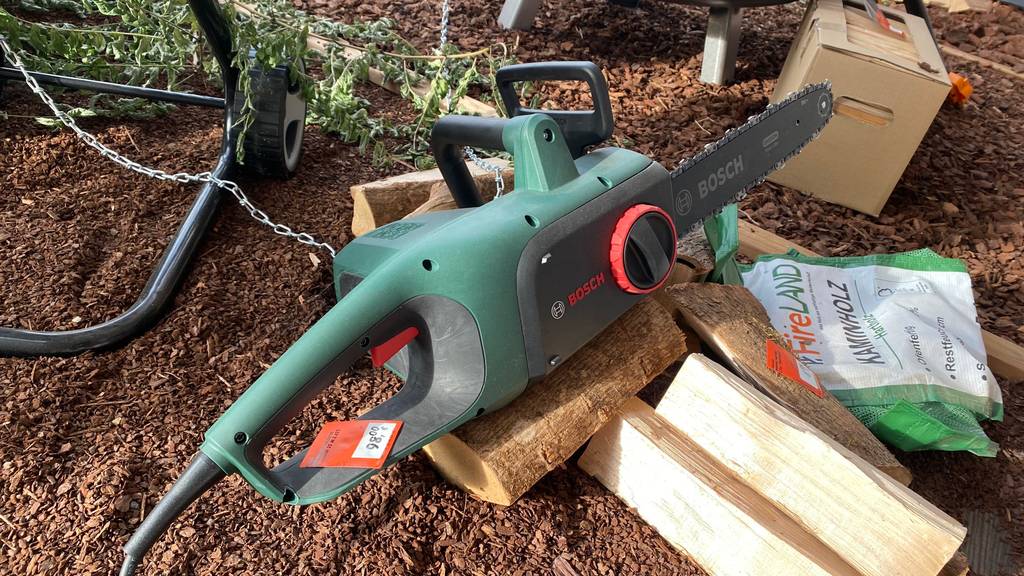Elektro-Kettensäge getestet: Nahaufnahme Griff und Motor auf mehreren Holzscheiten.