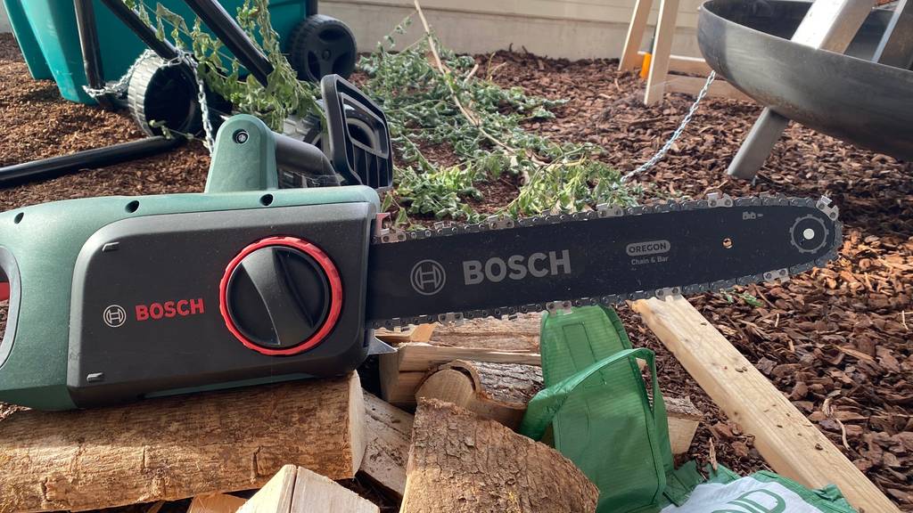 Im Test: Eine Elektro-Kettensäge liegt auf mehreren Holzscheiten auf dem Boden.