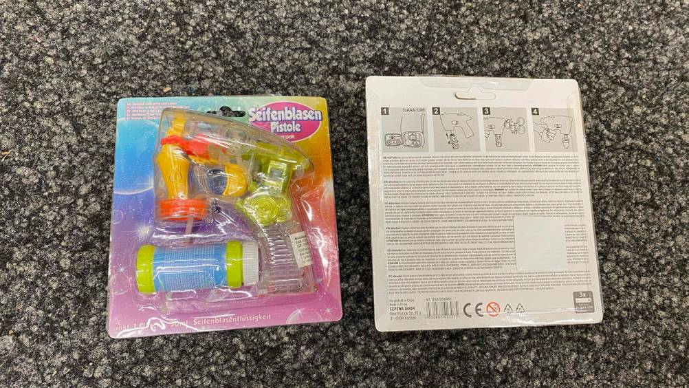 Im Test: Zwei verpackte Seifenblasenpistolen eine von vorne eine von hinten auf einem grauen Boden.