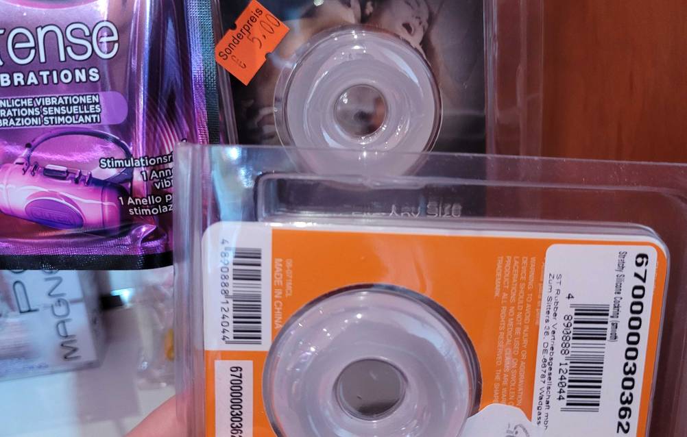 Im Test: Ein Penisring in seiner Verpackung vor anderen im Regal.