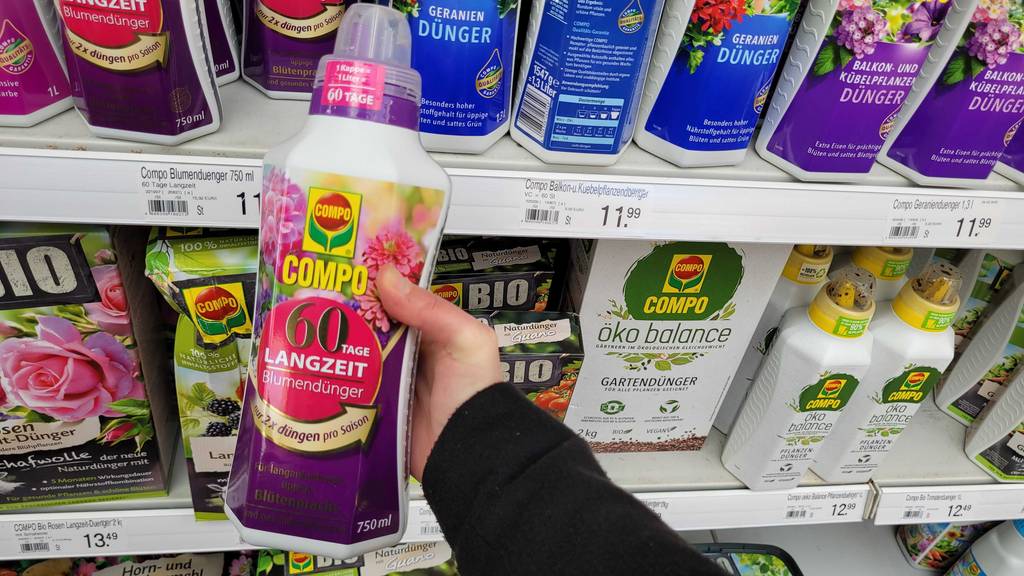 Eine Flasche des getesteten Langzeitdüngers wird in der Hand vor einem Regal gehalten.