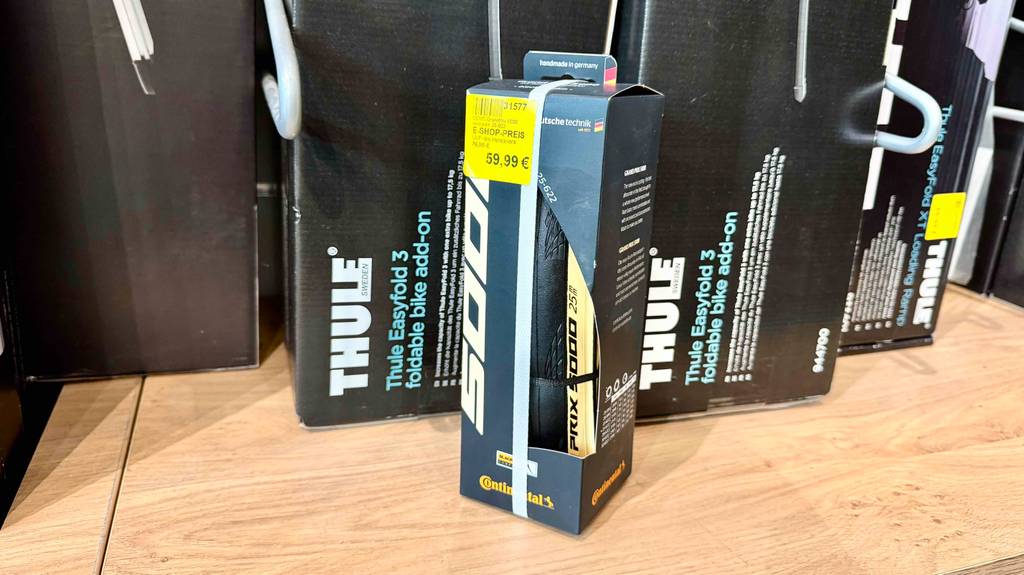 Eine Verpackung mit dem getesteten Rennrad-Reifen (25-622) steht vor einem Regal mit Fahrradständern.