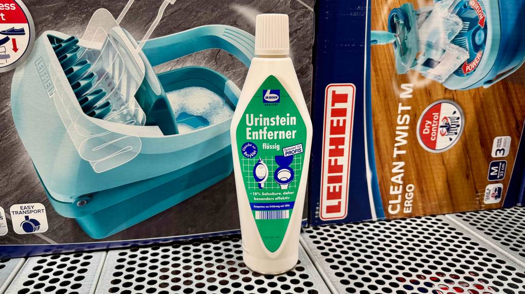Der getestete Urinsteinentferner steht vor zwei Verpackungen mit Bodenreiniger-Sets.