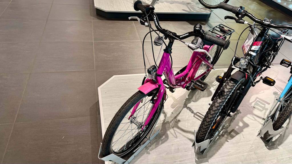Ansicht von schräg oben auf das pinkfarbene Mädchenfahrrad 20 Zoll im Test, das neben weiteren Fahrrädern auf einem Podest im Geschäft steht.
