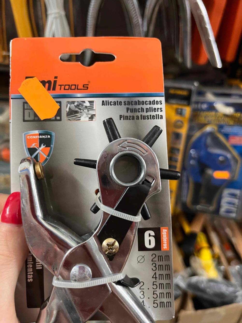 Revolverlochzange im Test: Eine Hand hält eine verpackte Zange, im Hintergrund mehrere Zangen
