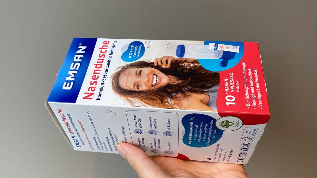 Nasendusche im Test: Eine Hand hält eine Packung Nasendusche seitlich vor einen grauen Hintergrund