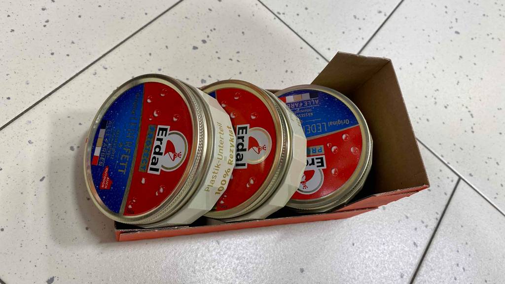 Lederfett im Test: drei Döschen Lederfett in einem Pappkarton auf einem Boden.