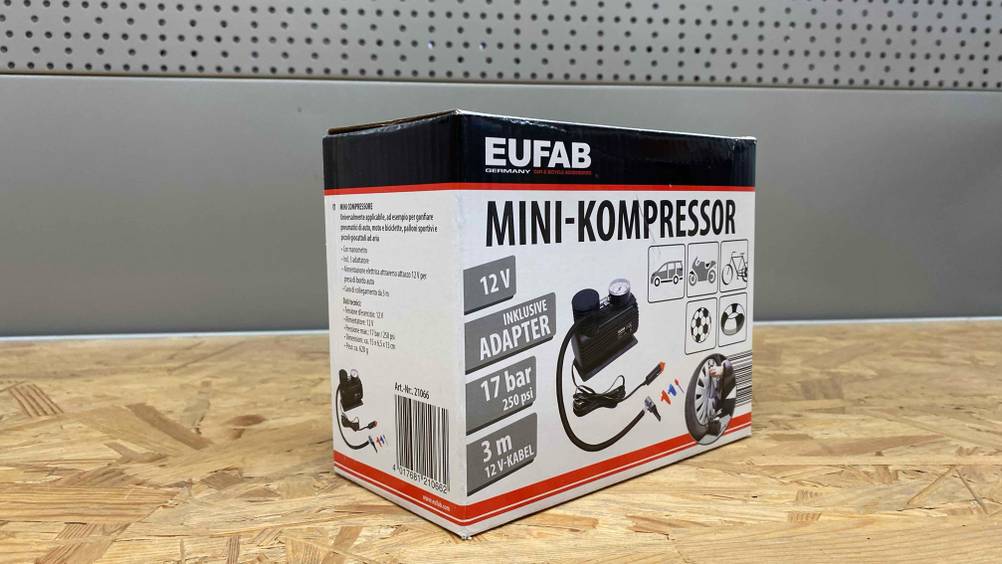 12V-Kompressor getestet: Vor einer grauen Wand auf einer Holzfläche steht ein verpackter 12V-Kompressor.