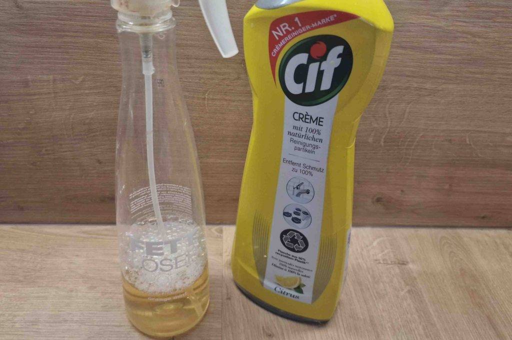 Eine Flasche getesteter Fettlöser steht neben einem anderen Reinigungsprodukt auf einer Holzfläche.
