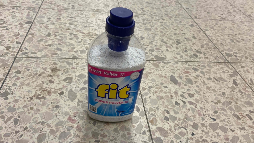 Eine Flasche des getesteten Spülmaschinenpulvers steht auf einem Fliesenboden.