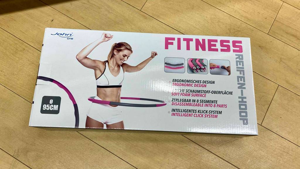 Im Test: Ein Hula Hoop Reifen in Originalverpackung auf einem Holzboden liegend.