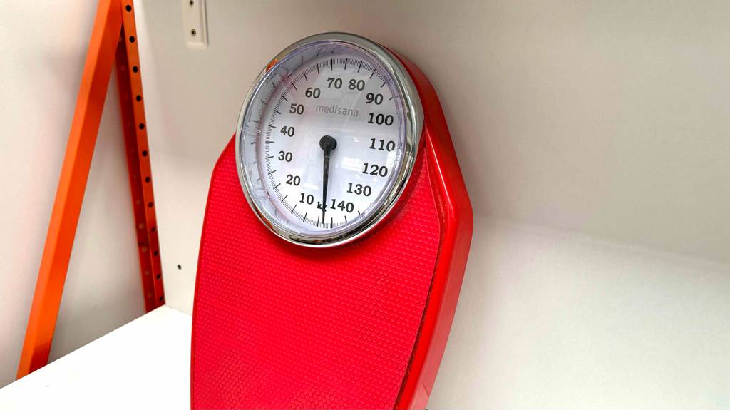 Analoge-Personenwaage-Test: eine rote analoge-Personenwaage bis 140 kg ist an einer weißen Wand angelehnt.
