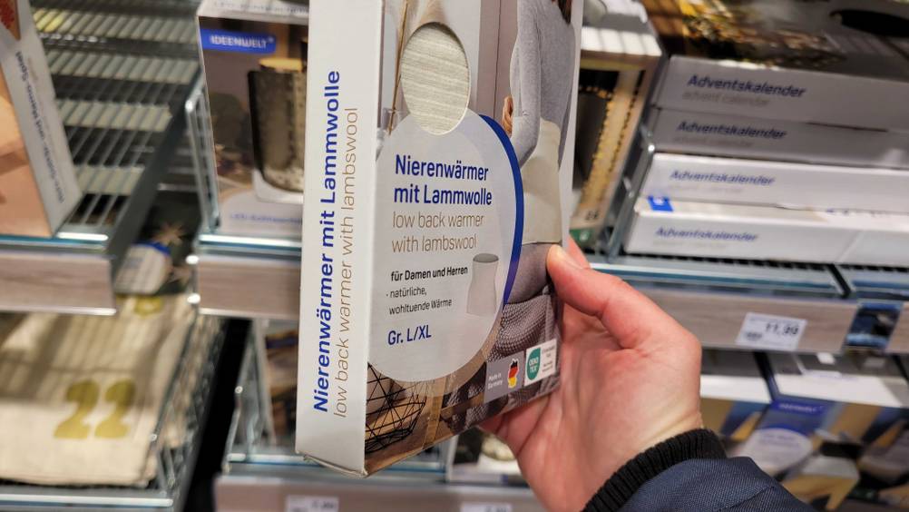 Nierenwärmer getestet: eine Packung Nierenwärmer in der Größe L/XL wird vor einem Regal gehalten.