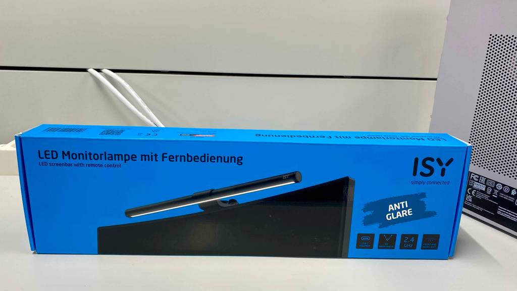 Auf einem hellen Boden steht eine verpackte Monitor-Lampe.
