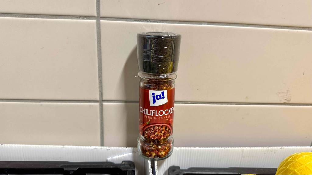 Ein Glas der getesteten Chiliflocken stehen auf offenen Kartons.