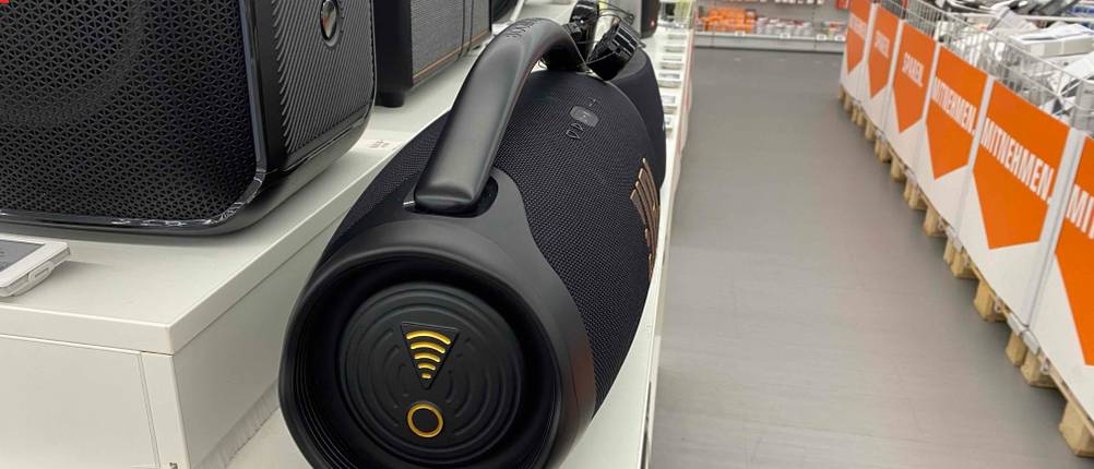 Im Test: Ein WLAN-Lautsprecher von der Seite neben anderen Produkten in einer Austellungsfläche.