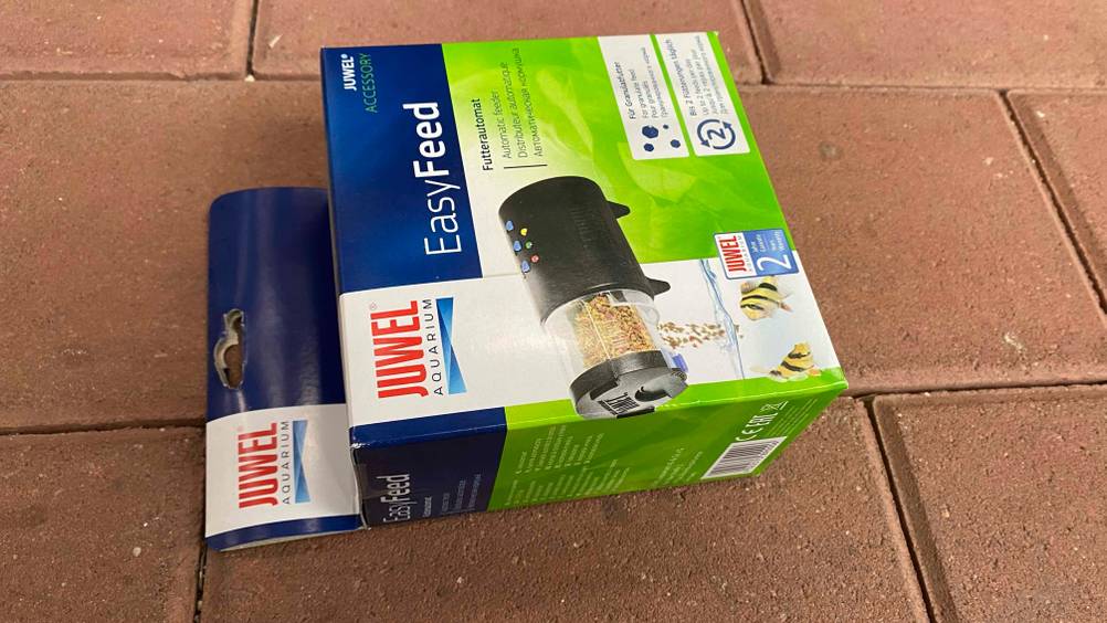 Futterautomat-Aquarium im Test: eine verschlossene Verpackung eines Futterautomaten für Granulatfutter liegt auf einem Boden.