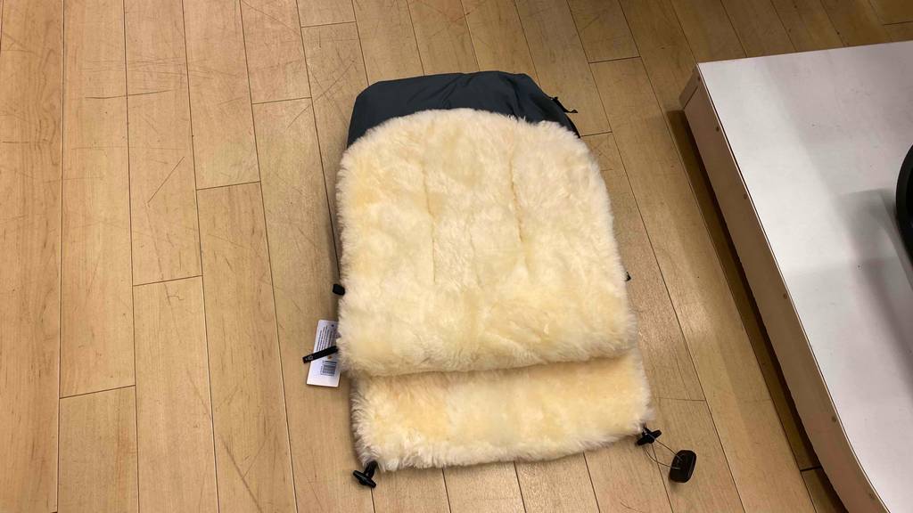Lammfell-Fußsack getestet: Ein Lammfell-Fußsack liegt auf einem Holzboden.