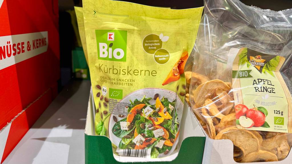 Getestet: Mehrere Packungen Bio-Kürbiskerne sind in einem Regal einsortiert, neben Apfelringen.