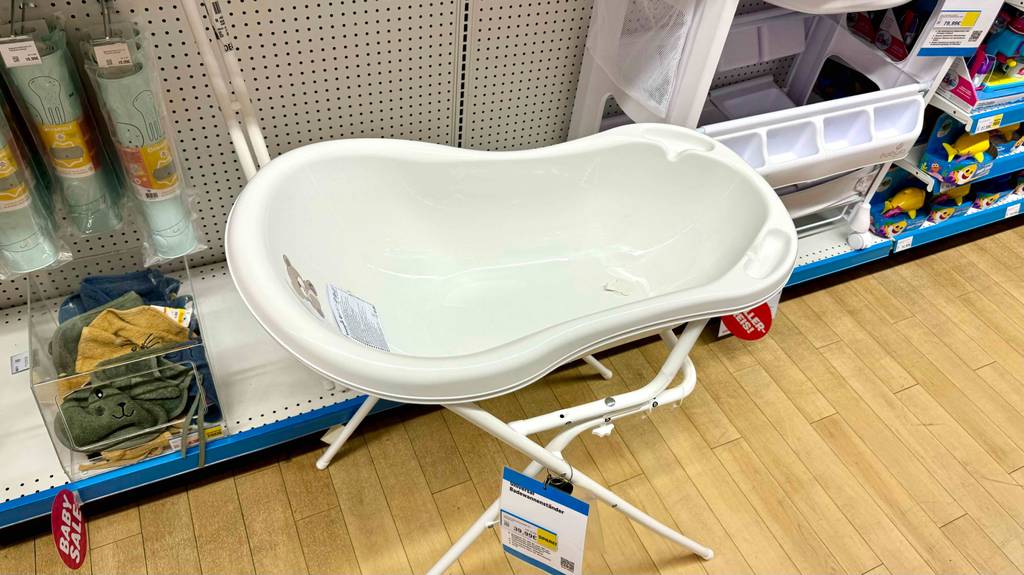 Eine weiße, getestete Babybadewanne mit Gestell steht vor einem Regal mit Blick auf den Innenraum und zwei Vertiefungen.