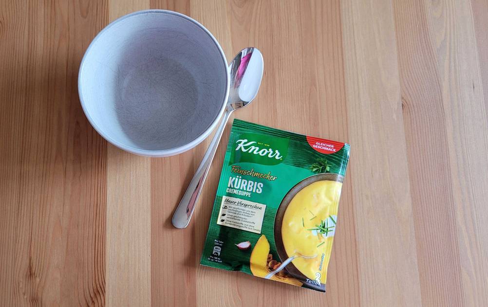 Kürbissuppe im Test: Eine Schüssel, ein Löffel und eine Packung Suppe auf einer Holzoberfläche