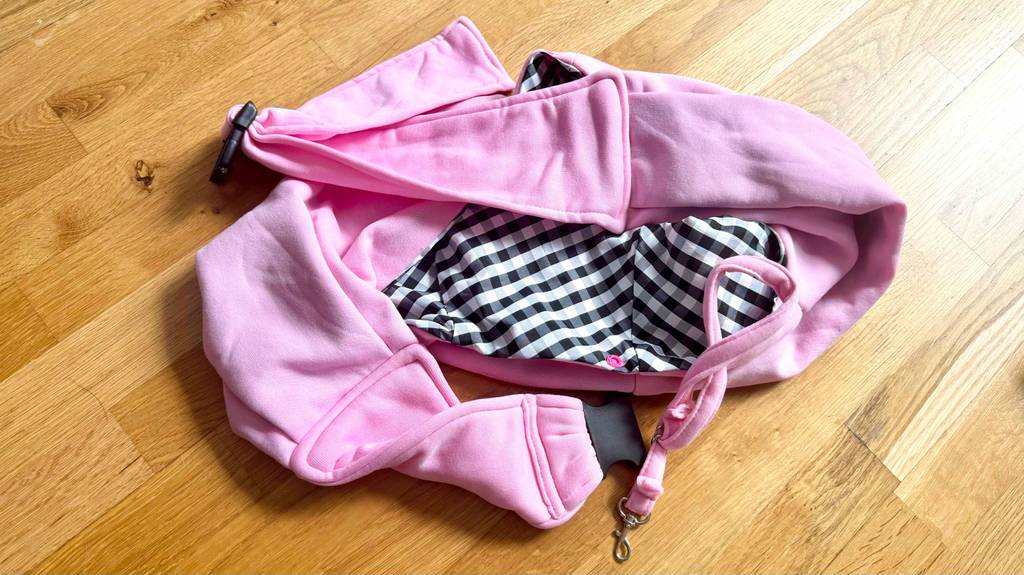 Getestete. Ein Hundetragetuch in der Farbe Rosa liegt auf einem Boden, mit einem karierten Muster auf der Innenseite.