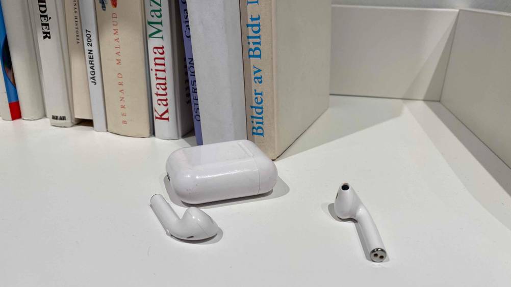 Kopfhörer getestet: zwei weiße In-Ear-Kopfhörer neben weißem Case vor Bücher platziert.