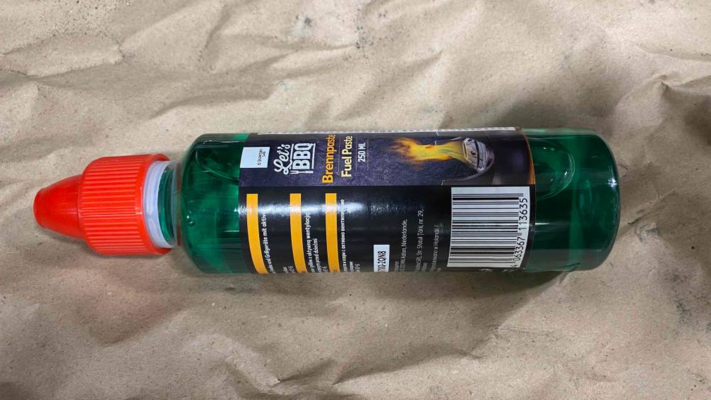 Brennpaste getestet: Eine Flasche horizontal auf einem Papier liegend.