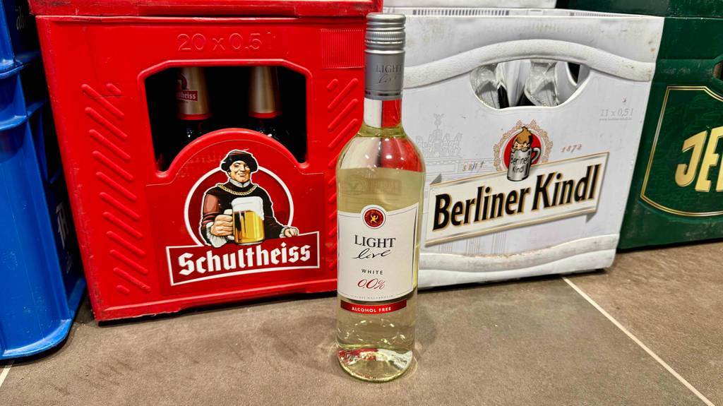 Die getestete Flasche alkoholfreier Weißwein steht auf einem Boden, vor Bierkisten.