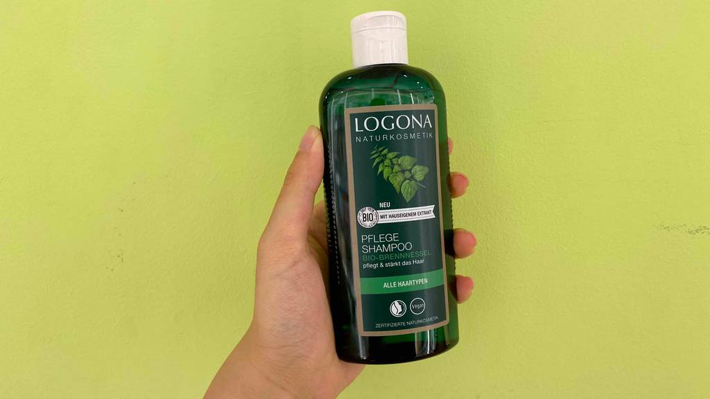 Brennessel-Shampoo im Test: Eine Hand hält eine Flasche vor grünen Hintergrund