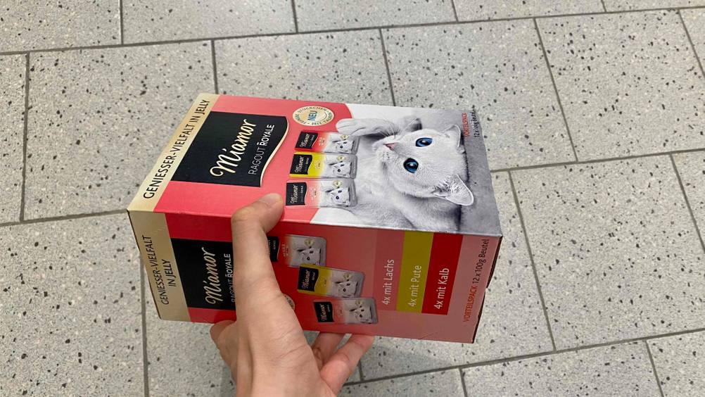 Im Test: Eine Hand hält eine Packung Miamor-Katzenfutter seitlich vor einen hellen Boden