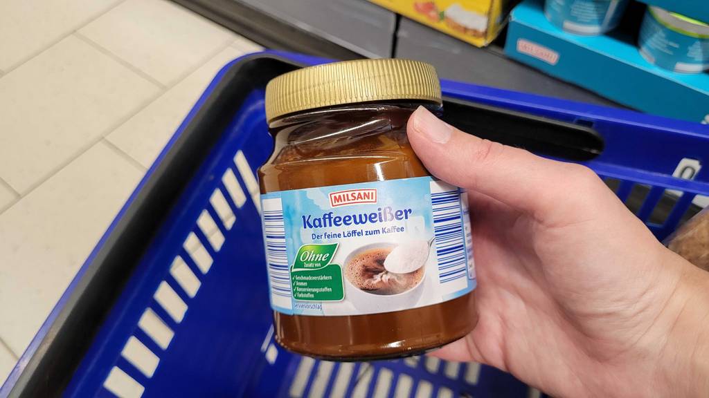 Im Test: Eine Hand hält einen Kaffeeweißer hoch, im Hintergrund ein Einkaufskorb