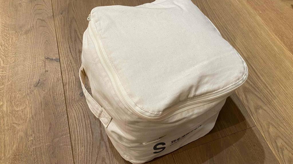 Bettdecke im Test: Bettdecke in einem cremeweißen Beutel eingepackt steht auf einem Boden.