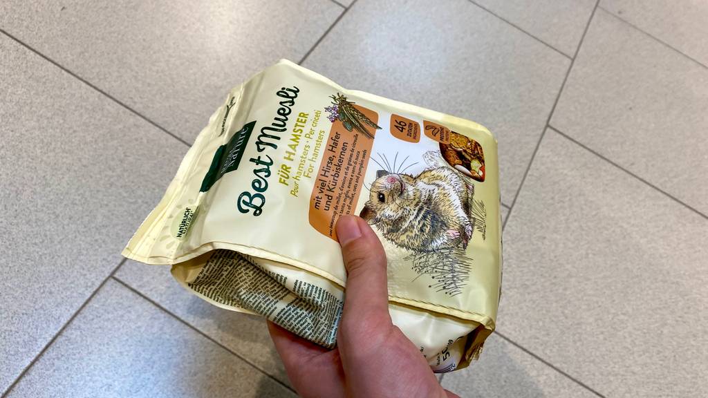 Hamsterfutter getestet: Eine Hand hält eine Packung Hamsterfutter vor Fließen