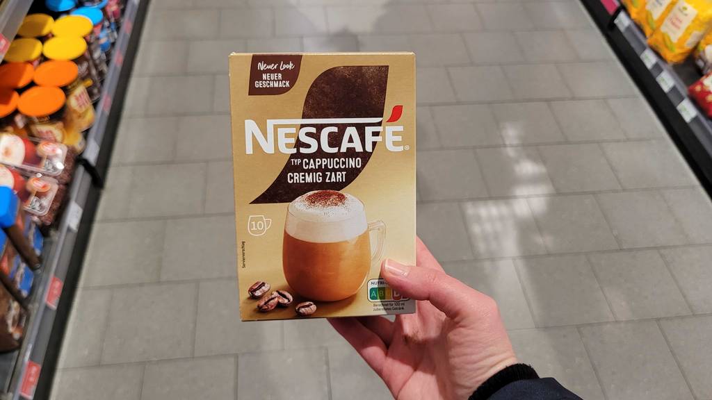 Eine Packung getesteter Instant-Cappuccino wird in der Hand gehalten.