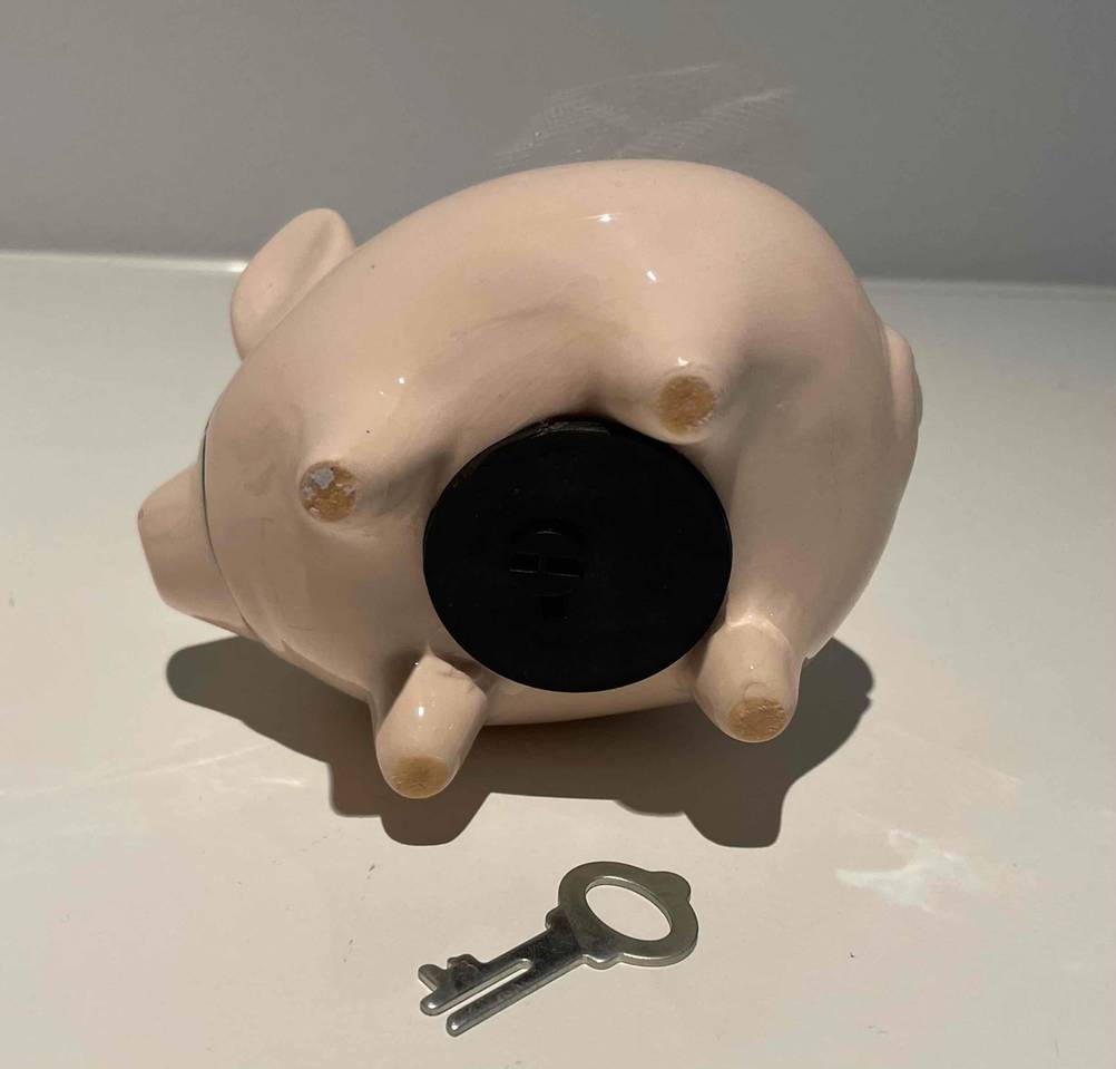Unterseite eines getesteten Sparschweins mit Schlüssel auf einer hellen Fläche.