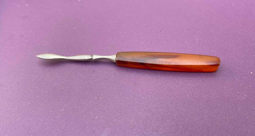Nagelhautschieber getestet: Nagelhautschieber liegt horizontal auf einer violettfarbenen Fläche mit einer spitz zulaufenden Spitze und braunem Griff.