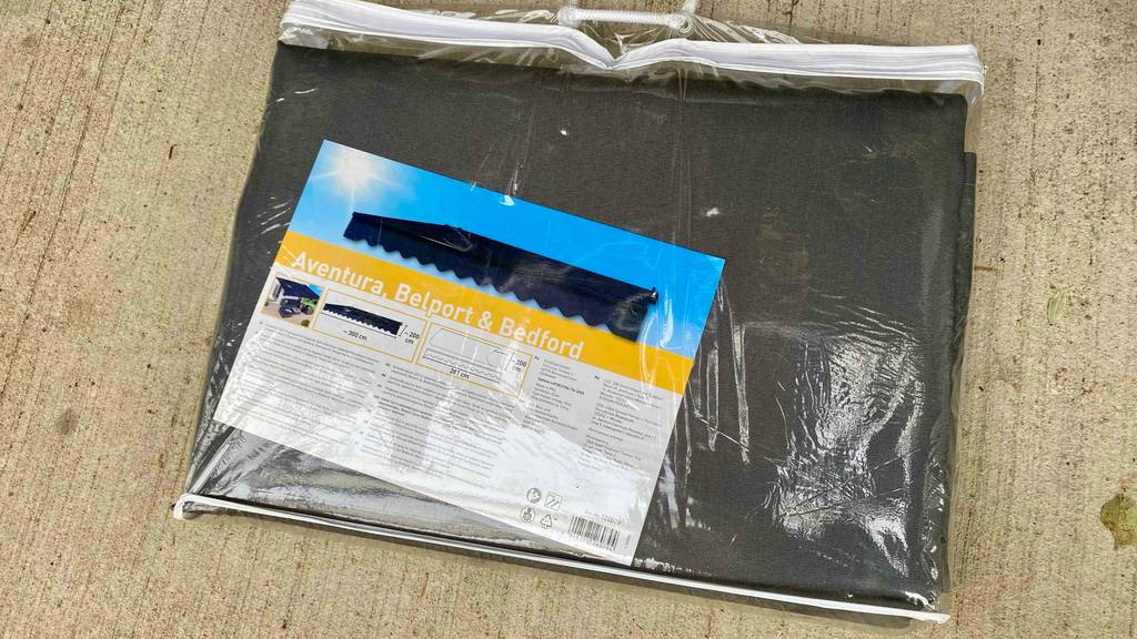 Ein getesteter Markisenstoff in Grau liegt in der Tragetrasche auf dem Boden.