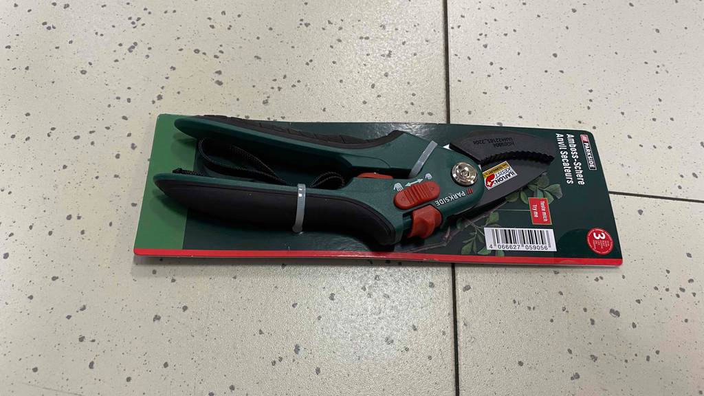 Auf einem Steinboden liegt eine getestete Amboss-Gartenschere in Originalverpackung