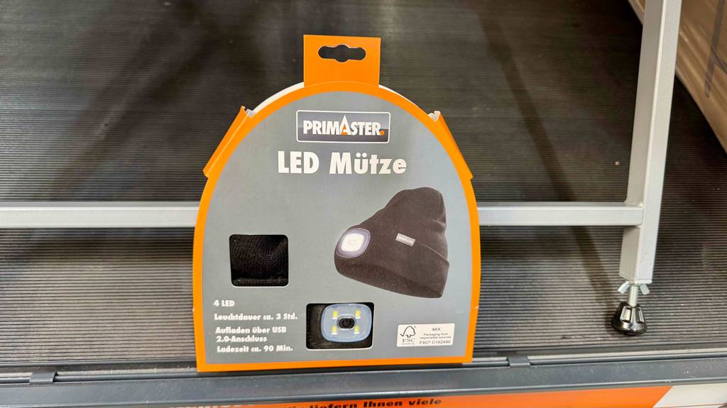 LED-Mützen im Test: Ein schwarzes Modell von Primaster befindet sich ein einem grau-orangefarbenen Verpackungskarton vor einem Regal.